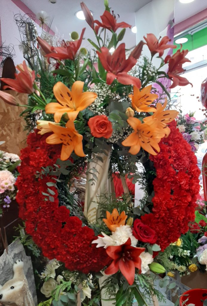 Corona funeraria Ninos , compuesta de liliun naranja y rojos ,clavel rojo y hoja de eucalipto.
