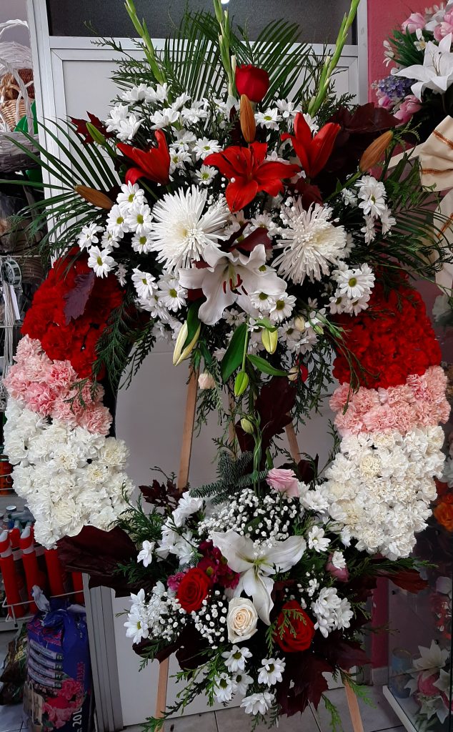 Corona funeraria de claveles , varios colores claveles rojos ,rosas y blancos, cabeceros con liliun blanco y rojo , margarita blanca, y media docena de rosas rojas y blancas