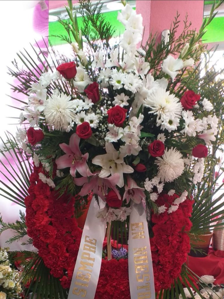 Corona  funeraria de flores ,con claveles rojos y en la parte superior liliun rosa anastasias blancas y rosas rojas
